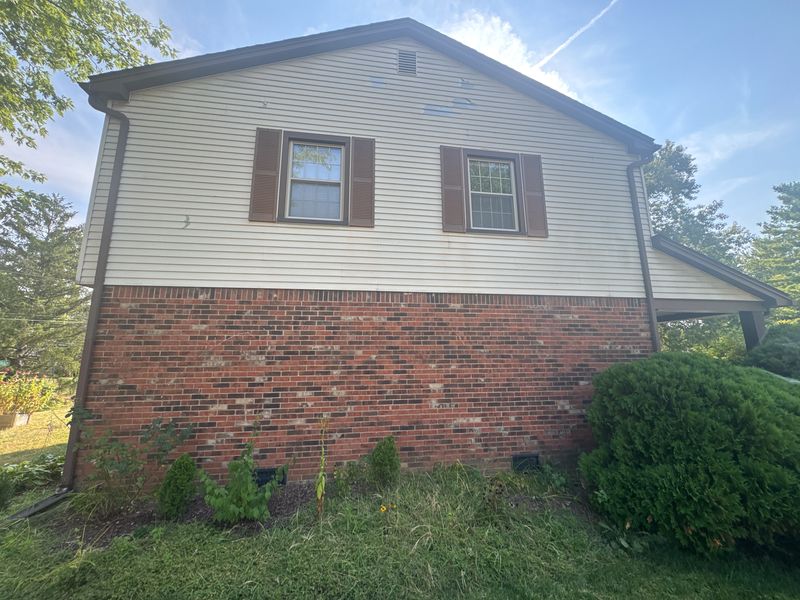 The gable end before painting: tan vinyl siding, brown shutters and a brown downspout over red brick